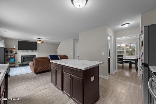 kitchen with freestanding refrigerator, dark brown cabinetry, light wood finished floors, and ceiling fan with notable chandelier