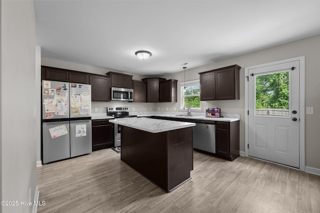 kitchen featuring appliances with stainless steel finishes, hanging light fixtures, a center island, light wood-type flooring, and dark brown cabinets