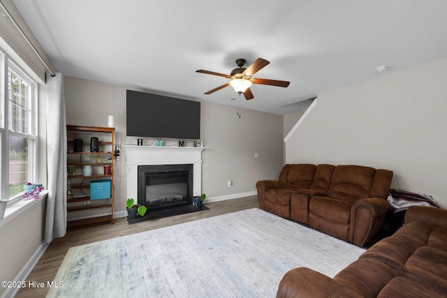 living room with baseboards, a fireplace with flush hearth, ceiling fan, and wood finished floors