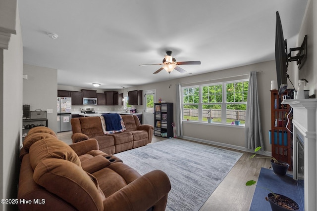 living area with baseboards, ceiling fan, a fireplace, and light wood finished floors
