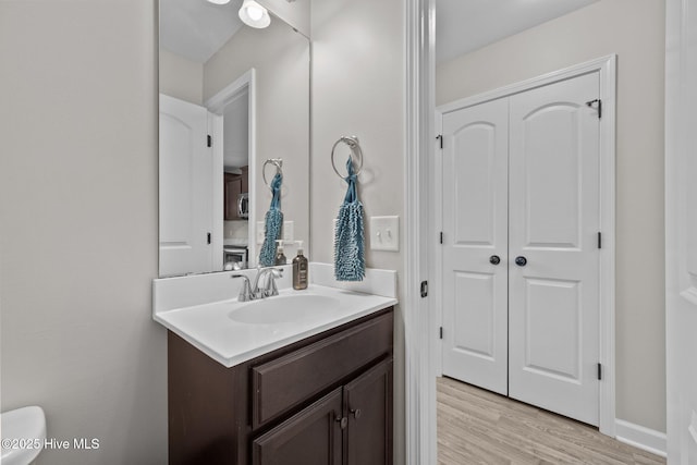 half bathroom with vanity, wood finished floors, and toilet
