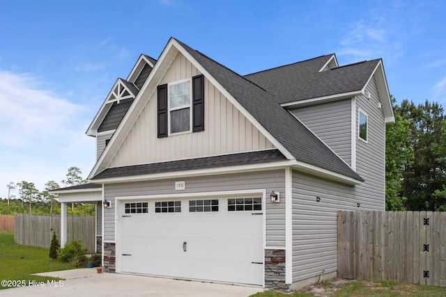 exterior space featuring fence, stone siding, board and batten siding, concrete driveway, and an attached garage