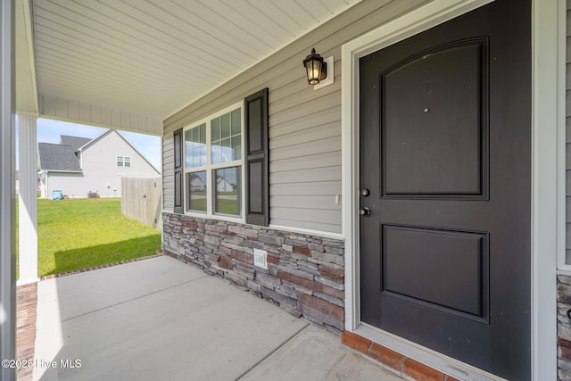 doorway to property featuring a lawn, covered porch, and stone siding