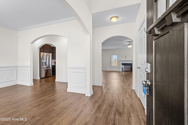 entryway featuring wainscoting, ornamental molding, a ceiling fan, a lit fireplace, and dark wood-style floors