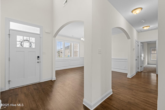 foyer entrance with arched walkways, baseboards, visible vents, and dark wood-type flooring