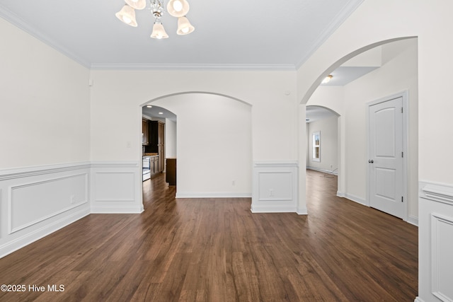 spare room featuring wood finished floors, a wainscoted wall, baseboards, a notable chandelier, and ornamental molding