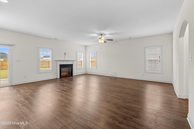 unfurnished living room with baseboards, a ceiling fan, dark wood-type flooring, and a wealth of natural light