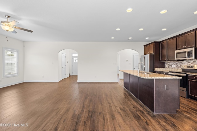 kitchen featuring dark brown cabinetry, open floor plan, a center island with sink, a ceiling fan, and stainless steel appliances