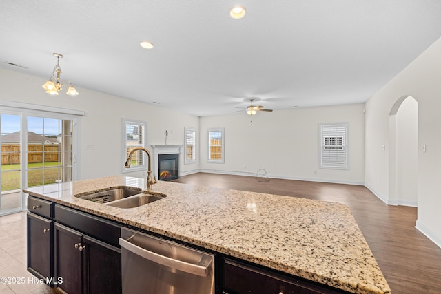 kitchen featuring a fireplace with flush hearth, stainless steel dishwasher, a sink, ceiling fan with notable chandelier, and open floor plan