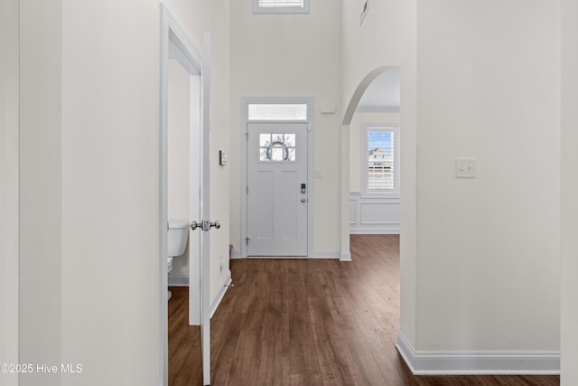 entryway featuring dark wood-style flooring, arched walkways, baseboards, and a towering ceiling