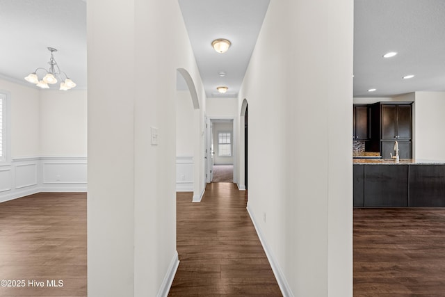 hallway with arched walkways, dark wood finished floors, a chandelier, and recessed lighting