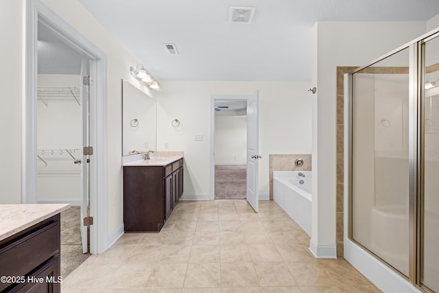 bathroom with vanity, a walk in closet, a stall shower, and visible vents