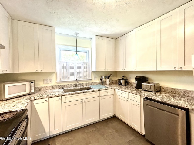 kitchen with hanging light fixtures, light stone counters, a sink, stainless steel appliances, and white cabinetry