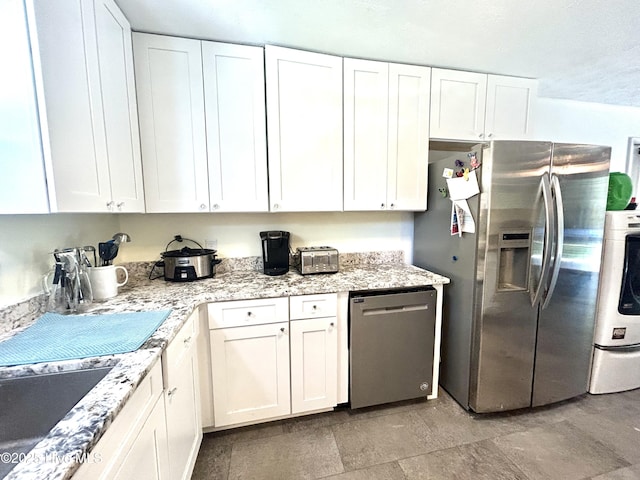kitchen with washing machine and clothes dryer, white cabinets, appliances with stainless steel finishes, and light stone countertops