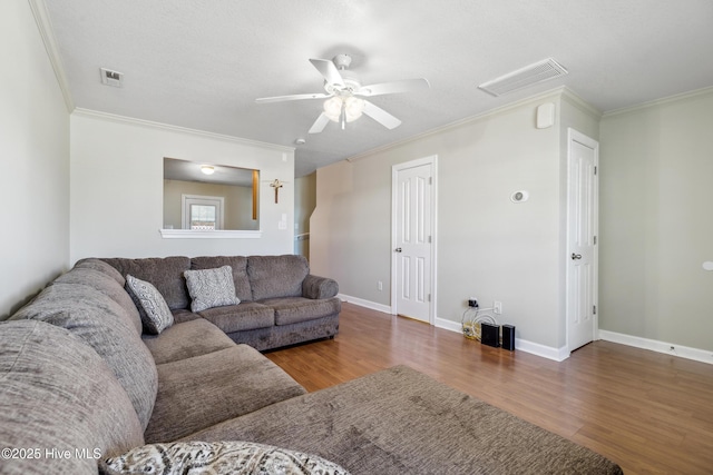 living area featuring a ceiling fan, visible vents, wood finished floors, baseboards, and ornamental molding