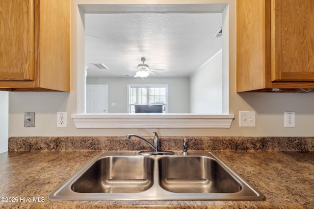 kitchen featuring brown cabinetry, a sink, a ceiling fan, and visible vents