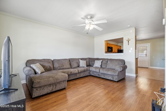 living room featuring light wood-type flooring, a ceiling fan, baseboards, and ornamental molding