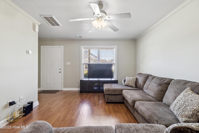 living area with crown molding, ceiling fan, wood finished floors, and visible vents