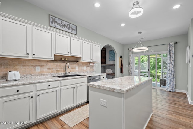 kitchen featuring a sink, arched walkways, white cabinetry, decorative backsplash, and a kitchen island