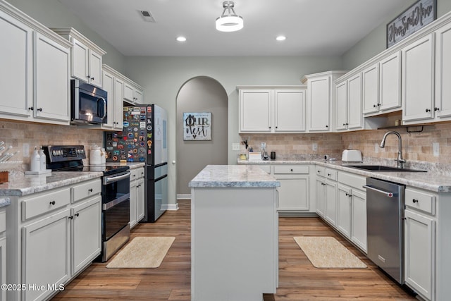 kitchen with a kitchen island, tasteful backsplash, a sink, stainless steel appliances, and white cabinetry