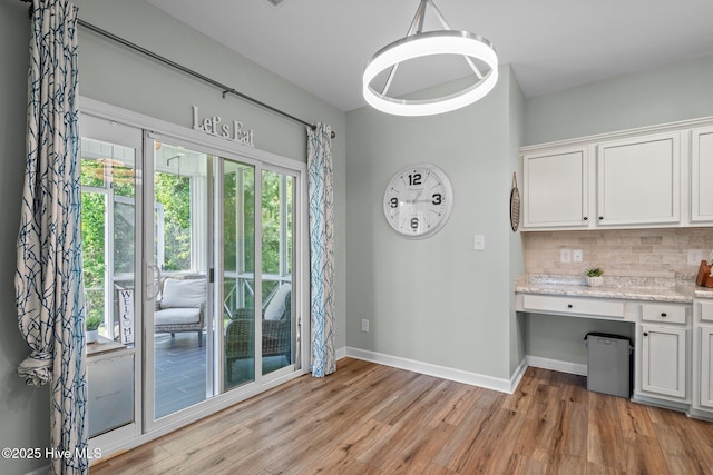 unfurnished dining area featuring built in study area, baseboards, and light wood finished floors