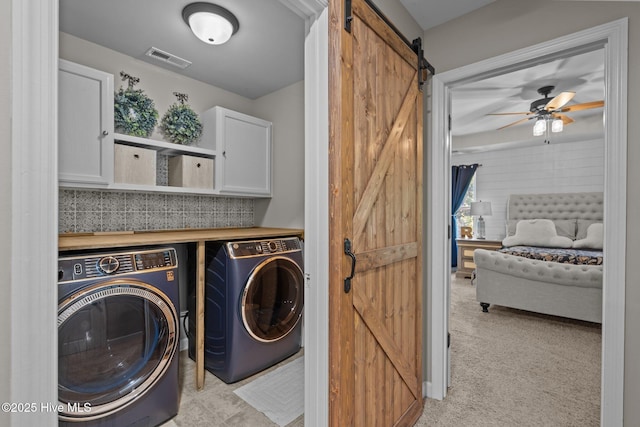 clothes washing area featuring ceiling fan, visible vents, washing machine and dryer, a barn door, and cabinet space