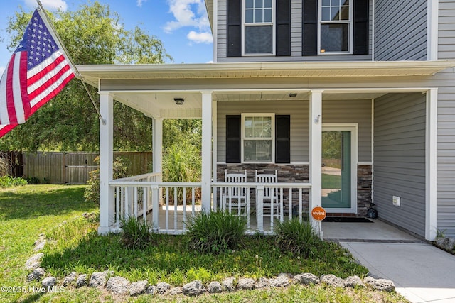 property entrance with a porch, a lawn, fence, and stone siding