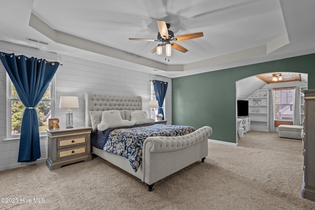 carpeted bedroom with arched walkways, a tray ceiling, visible vents, and a ceiling fan
