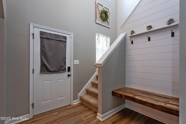 foyer featuring wooden walls, baseboards, stairway, and wood finished floors