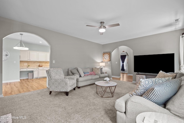 living room with a ceiling fan, light colored carpet, visible vents, arched walkways, and baseboards