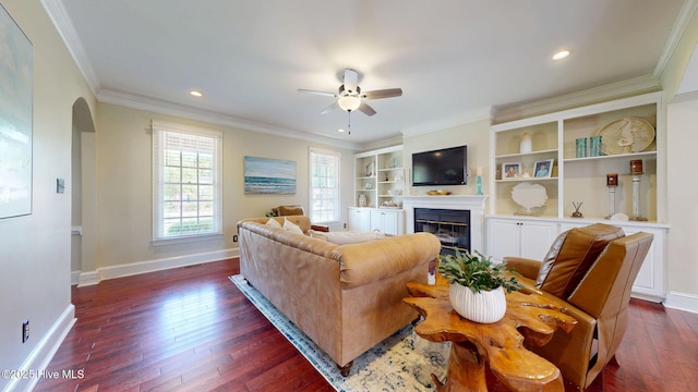 living room with a ceiling fan, crown molding, baseboards, dark wood-style floors, and a glass covered fireplace