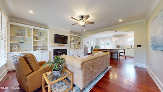 living room featuring a ceiling fan, visible vents, crown molding, a glass covered fireplace, and dark wood-type flooring