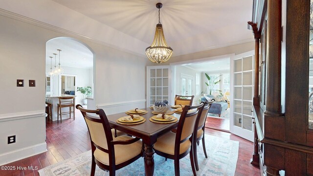 dining area featuring wood-type flooring, arched walkways, an inviting chandelier, and ornamental molding