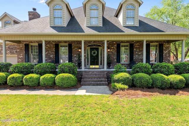 cape cod house featuring a porch, brick siding, and a front yard