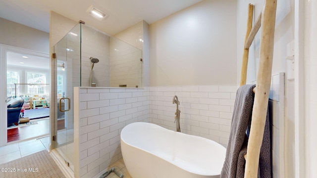 ensuite bathroom with wainscoting, tile patterned floors, a freestanding tub, tile walls, and a shower stall
