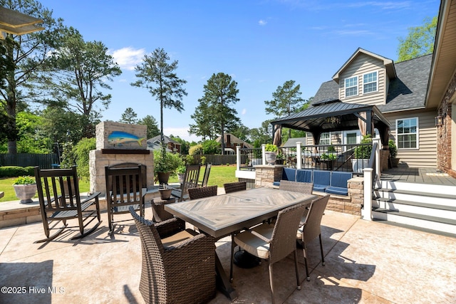 view of patio / terrace featuring an outdoor stone fireplace, outdoor dining area, fence, and a gazebo