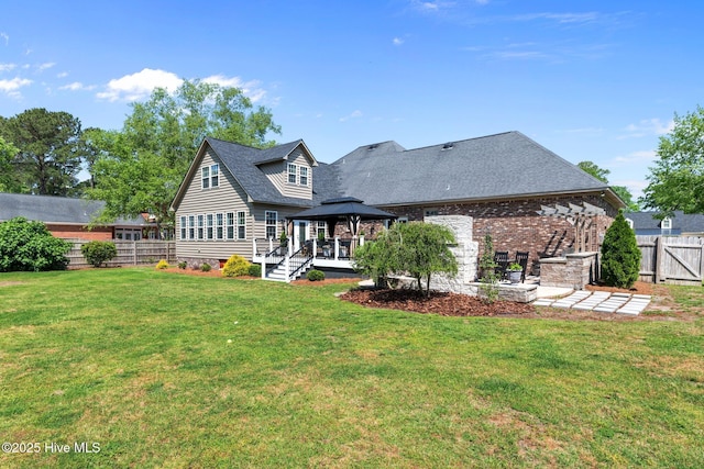 back of property with fence, roof with shingles, a gazebo, brick siding, and a yard
