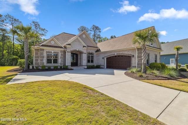 french country inspired facade with an attached garage, roof with shingles, a front yard, brick siding, and driveway