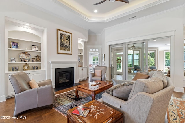living room featuring wood finished floors, visible vents, built in features, ceiling fan, and a fireplace with flush hearth
