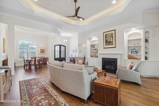 living area with ceiling fan with notable chandelier, wood finished floors, built in features, arched walkways, and a glass covered fireplace