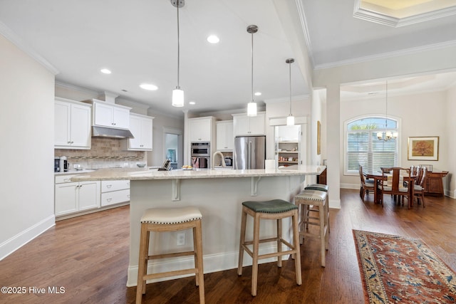 kitchen with stainless steel appliances, under cabinet range hood, a chandelier, crown molding, and decorative backsplash