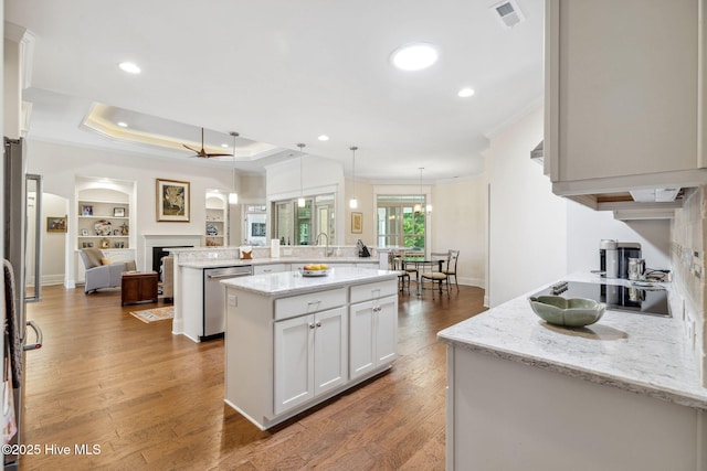 kitchen with an island with sink, white cabinets, stainless steel dishwasher, visible vents, and ornamental molding