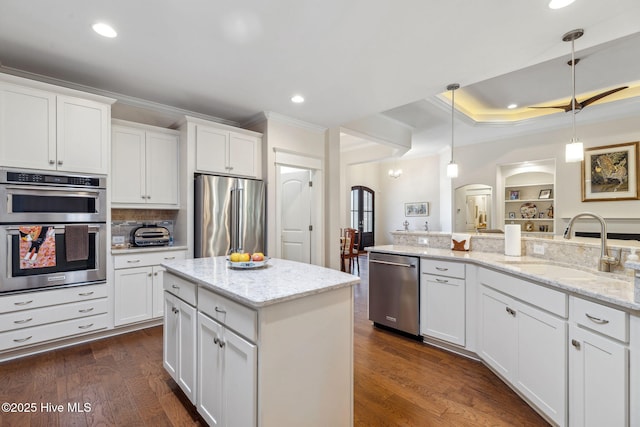kitchen with hanging light fixtures, a sink, stainless steel appliances, arched walkways, and ornamental molding