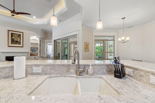 kitchen featuring ceiling fan with notable chandelier, a sink, pendant lighting, crown molding, and light stone counters