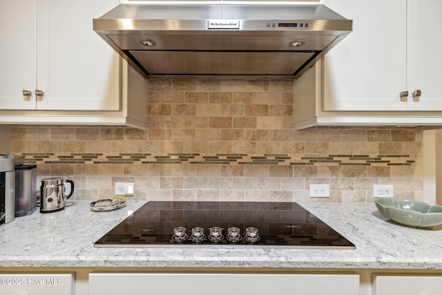kitchen featuring white cabinets, light stone countertops, exhaust hood, black electric cooktop, and decorative backsplash