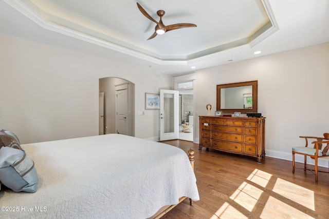 bedroom featuring wood finished floors, recessed lighting, arched walkways, a raised ceiling, and baseboards