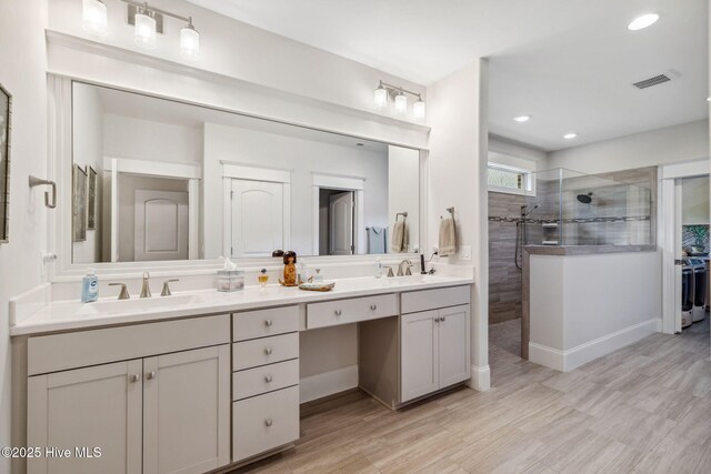 full bath with visible vents, a sink, a walk in shower, double vanity, and wood finished floors
