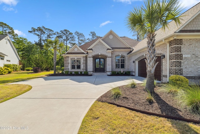 view of front of house featuring french doors, brick siding, an attached garage, concrete driveway, and a front lawn