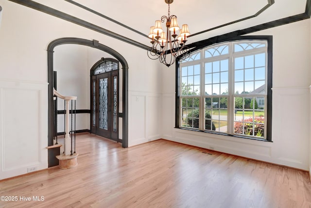 entrance foyer with arched walkways, light wood finished floors, and a decorative wall