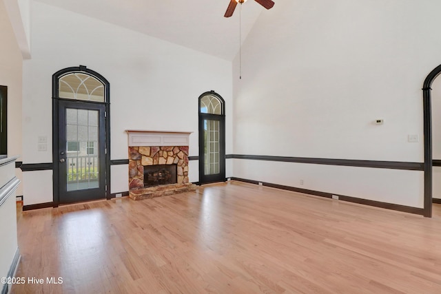 unfurnished living room featuring ceiling fan, a stone fireplace, high vaulted ceiling, baseboards, and light wood-style floors